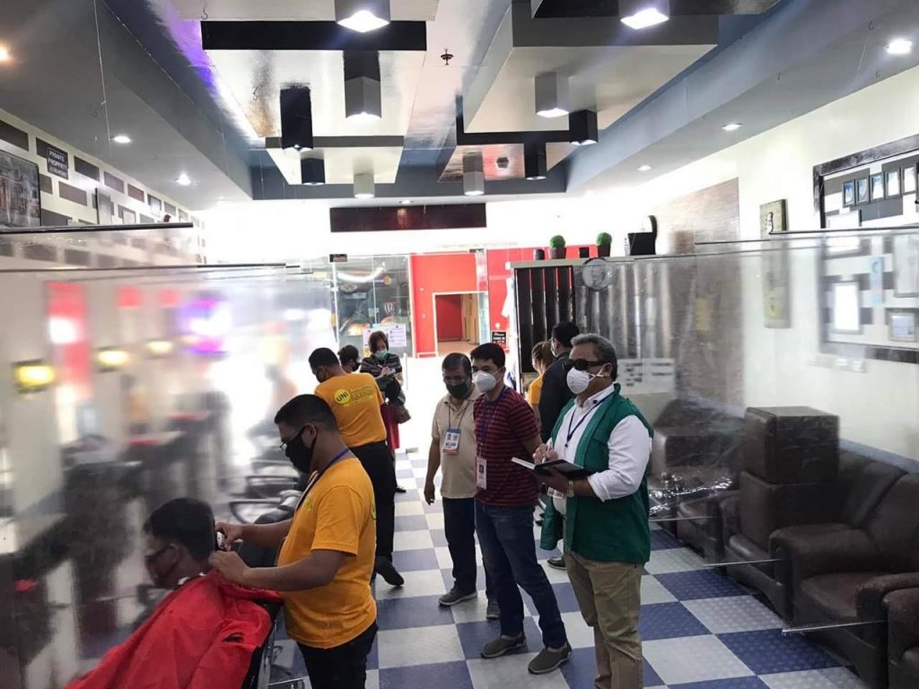 DTI inspectors inspecting a barber wearing a facemask service a client in a barbershop in a mall in Region 9