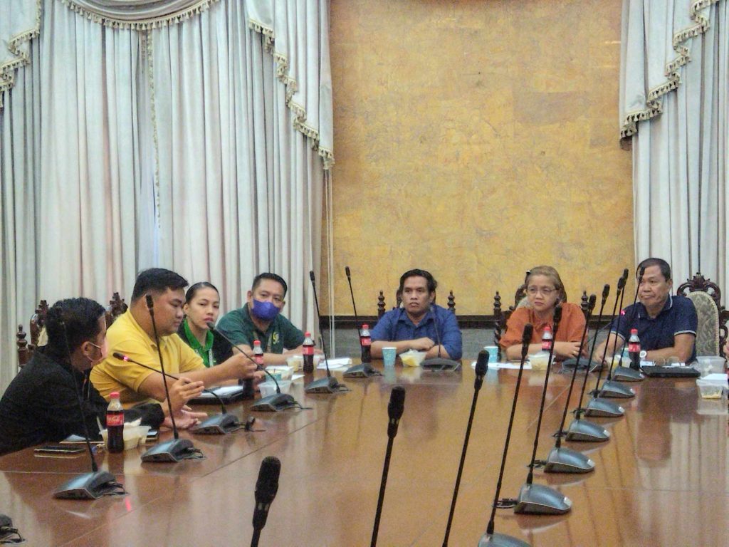 People seated at a conference table engaged in discussion, with microphones and drinks present.