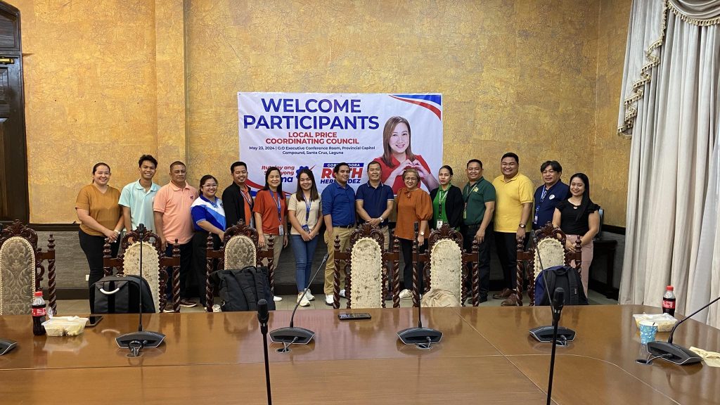 Group of people standing in front of a banner that reads "Welcome Participants Local Price Coordinating Council" in a conference room setting.