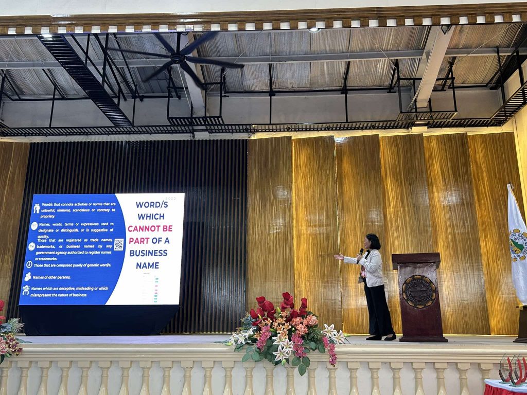 Speaker presenting guidelines on prohibited words for business names in a decorated venue.