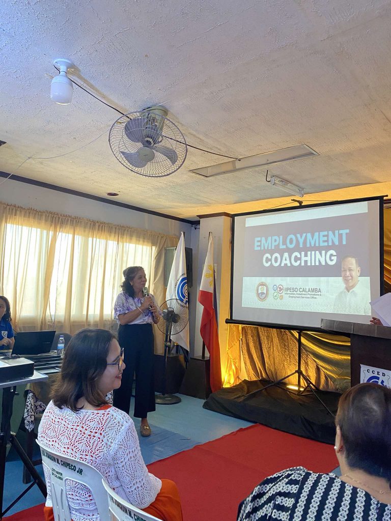 Speaker presenting at an employment coaching event, with a projector screen displaying the title "EMPLOYMENT COACHING."