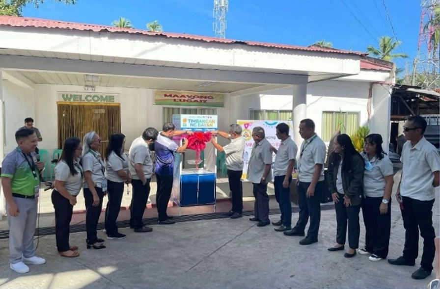 A group of DTI and local government officials gathered in front of a municipal building, unveiling a caged weighing scale labeled “Timbangan ng Bayan.”