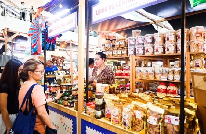 A vendor at Kultura Fest: Philippine Trade Fair in Festival Mall, Alabang, assists customers browsing a selection of locally made food products, including bottled spreads, snacks, and packaged delicacies. The booth, labeled "Likha ng Central Luzon," highlights regional specialties from Filipino MSMEs.