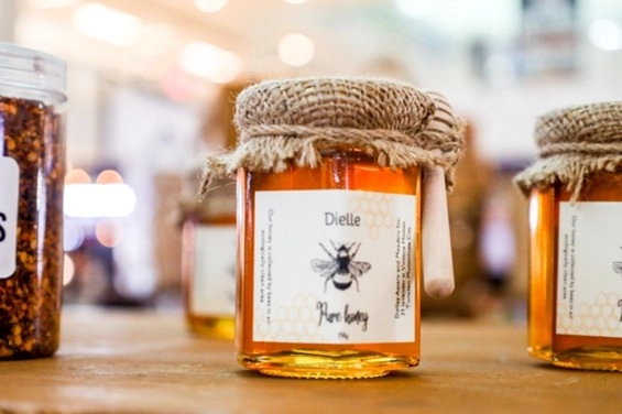 A jar of "Dielle" pure honey with a rustic jute-wrapped lid and wooden honey dipper is displayed at Kultura Fest: Philippine Trade Fair. The locally sourced product represents the artisanal quality and sustainability efforts of Filipino MSMEs.
