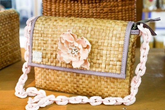 A stylish woven handbag with a pink floral embellishment and braided strap is featured at Kultura Fest: Philippine Trade Fair. The bag, made from native materials, highlights Filipino craftsmanship and eco-friendly fashion.