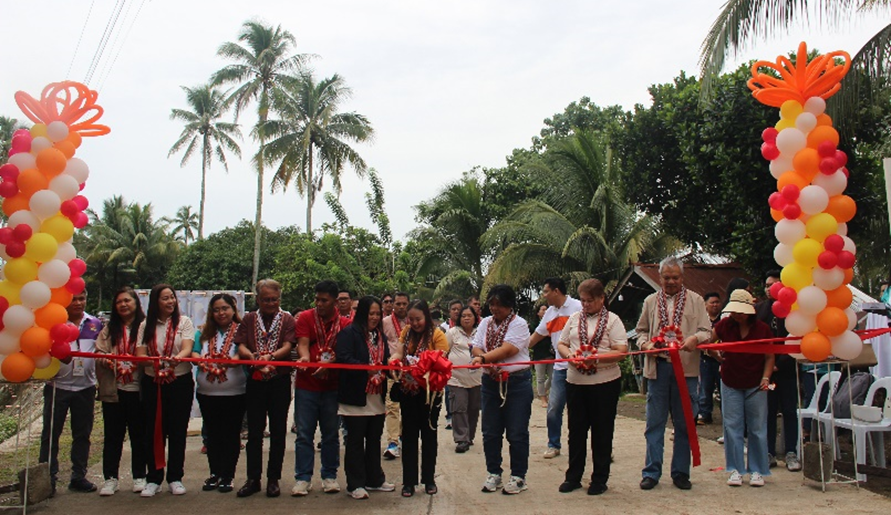 A ribbon-cutting ceremony for the PHP 30-million farm-to-market road improvement project in Lanao Del Norte, Philippines. The event features several individuals, including DTI RAPID Project Director and DTI Region 12 Director Flora Gabunales, standing in front of a decorated archway with balloons, holding a red ribbon. The project aims to improve market access for farmers and boost local incomes.