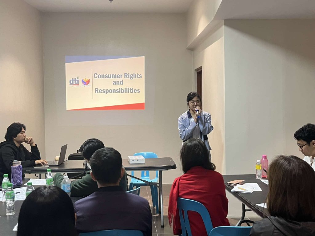 DTI seminar: Speaker at front of room, delivering a presentation about consumer rights and responsibilities. Audience seated.