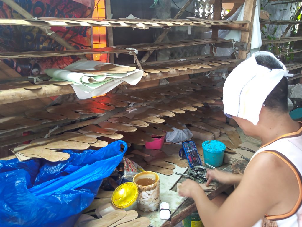 Footwear MSME worker crafting soles; wooden racks store materials.