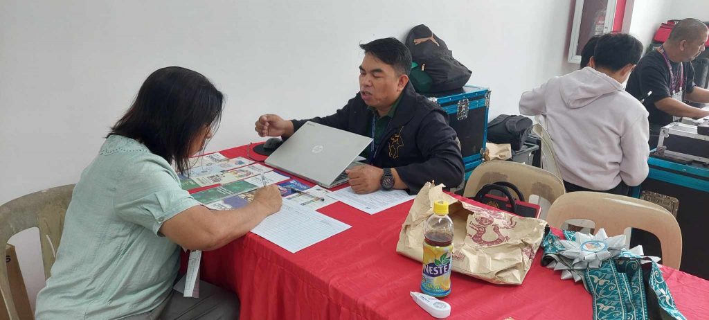 A DTI Region 4-A Rizal representative assisting a local business owner during the Pililla Business Conference 2025, with informational materials and a laptop on the table.