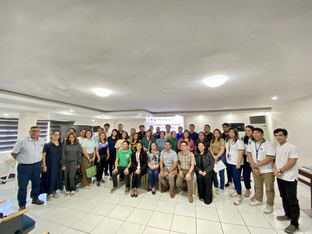 A large group of men and women pose together for a photo in a well-lit conference room, reflecting a collaborative atmosphere during the Chamber Management and Planning Workshop.