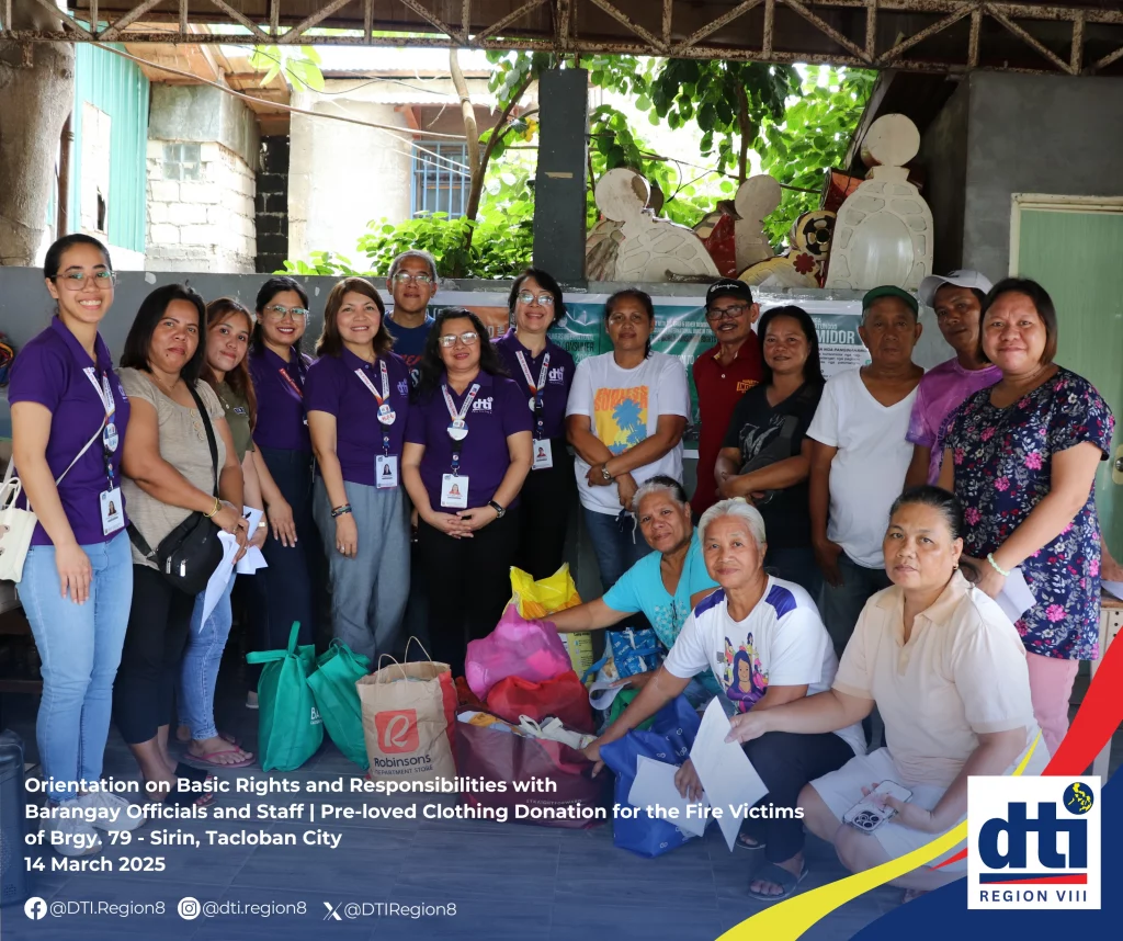 A group of DTI Region 8 staff wearing purple shirts poses alongside Barangay 79 Sirin officials and community members in Tacloban City. They are gathered around donated pre-loved clothing intended for local fire victims, taken on March 14, 2025, during an orientation on basic consumer rights and responsibilities.