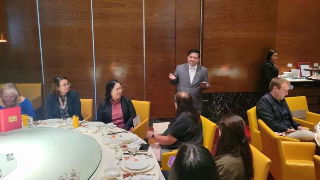 FTSO III Jeremiah C. Reyes, standing in a gray suit, delivers welcome remarks to a group of seated attendees around a round dining table in a wood-paneled room during a networking luncheon on March 12, 2025.