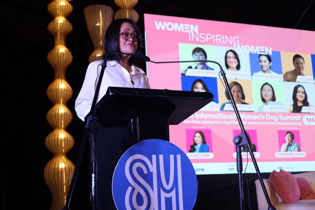 DTI-Regional Operations Group Undersecretary Blesila Lantayona delivering a speech during the International Women's Day Summit at the Samsung Hall, SM Aura. Behind her is a lit presentation entitled, "Women Inspiring Women".