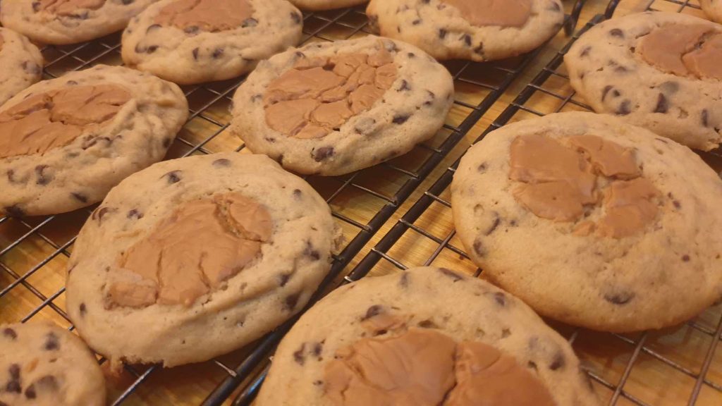 Freshly baked chocolate chip cookies topped with peanut butter cups on a cooling rack.