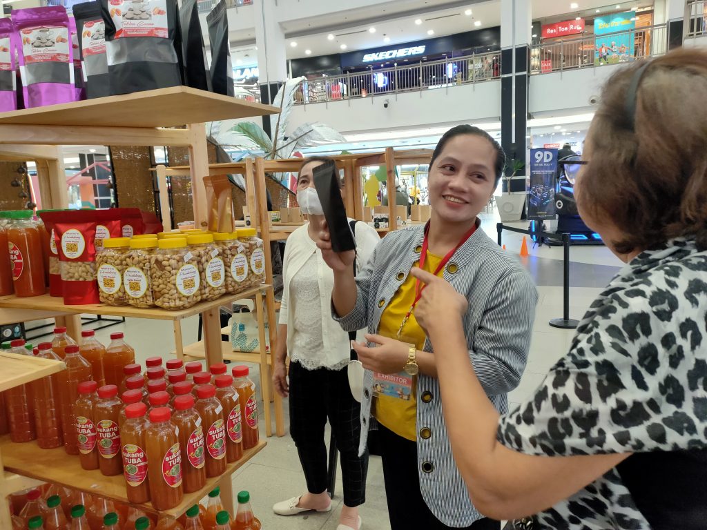 Ms. Rosemarie Guzman selling local tuba and snacks at a mall booth. Smiling at customer.