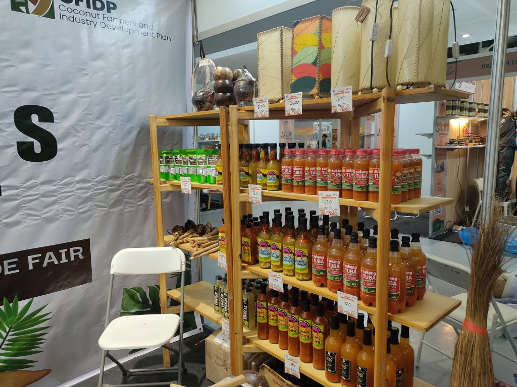 Shelves showcasing coconut vinegar and native crafts at a trade fair. "CFIDP Coconut Farmers" banner visible.