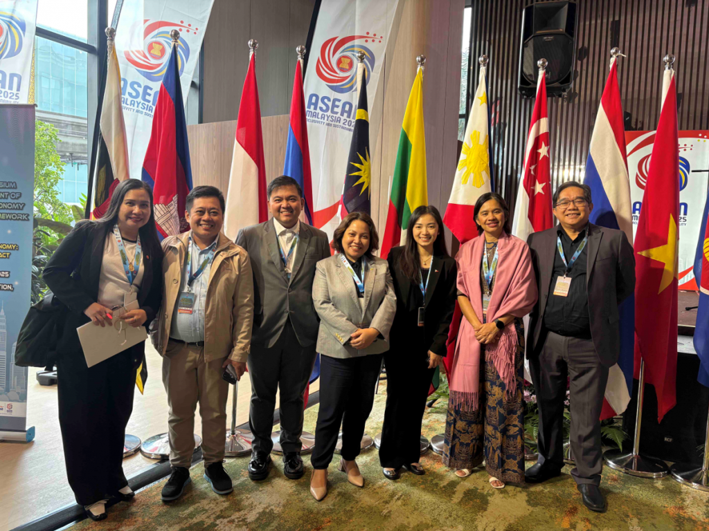 A group of seven individuals stands in front of several ASEAN member flags, all wearing business or semi-formal attire and smiling for the camera. They appear to be representatives from cultural and government organizations, gathered at an event.