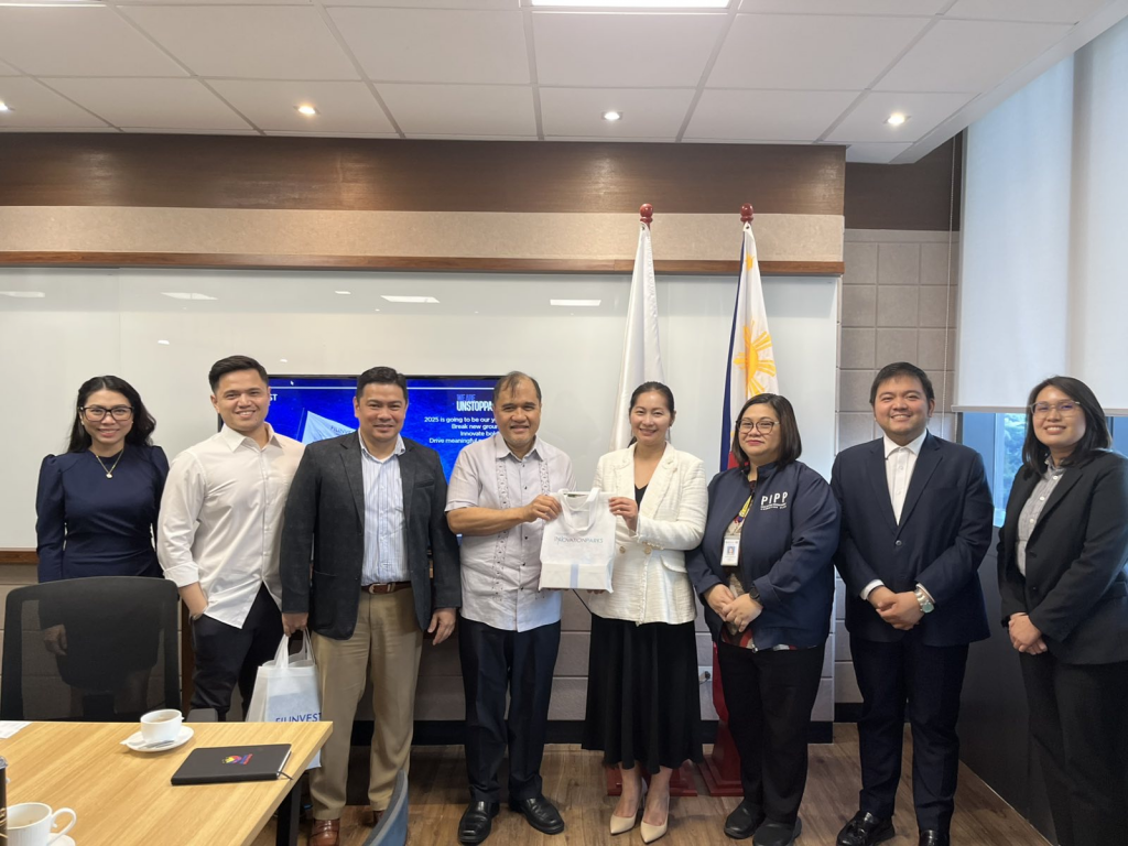 A group of seven people from DTI-FTSC and Filinvest stand together in a meeting room, wearing business attire and smiling at the camera. One person holds a document, and the Philippine flags are visible in the background.