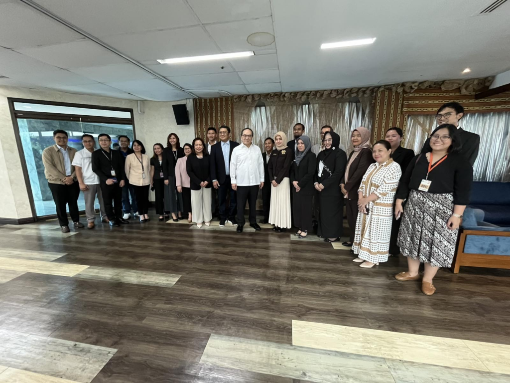 A group of individuals from PTIC in Jakarta and the Philippine National Oil Company (PNOC) stand together in a meeting room, wearing business attire and posing for a photo. The room features large windows and curtains in the background. The meeting took place in November 2024.