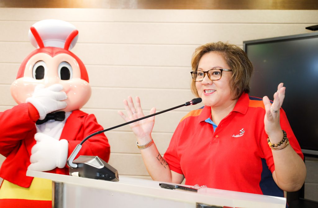 Eloise Anne Siccion, Jollibee AVP, speaks at a podium with the Jollibee mascot beside her.