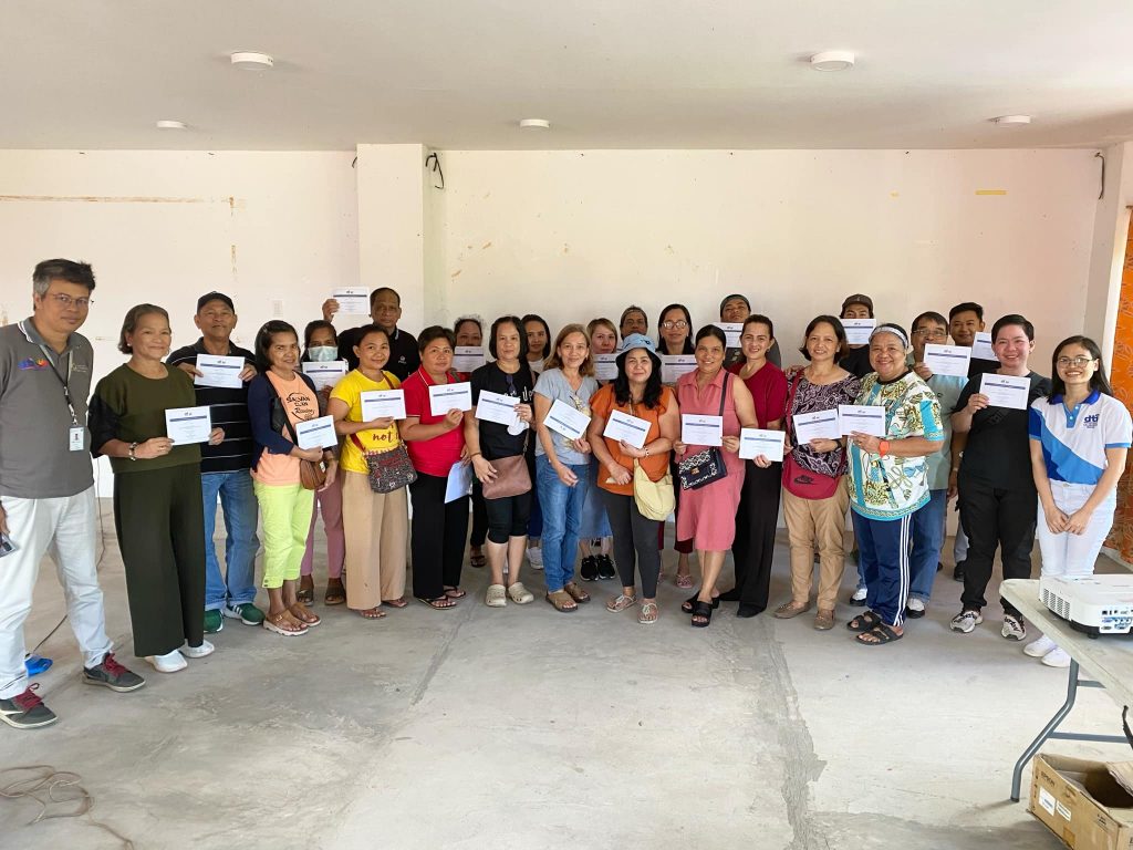 Participants, mostly local MSMEs from Luisiana, Laguna, pose for a group photo with seminar organizers after attending the DTI-Laguna session on SBCorp Loan Programs and Consumer Education. Many attendees are holding up certificates or documents received during the event.