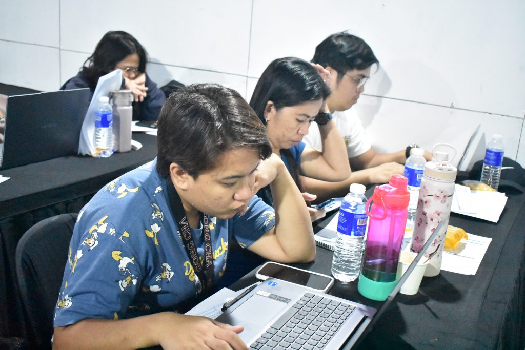 Several people are sitting at a table working on laptops. Water bottles are also on the table.
