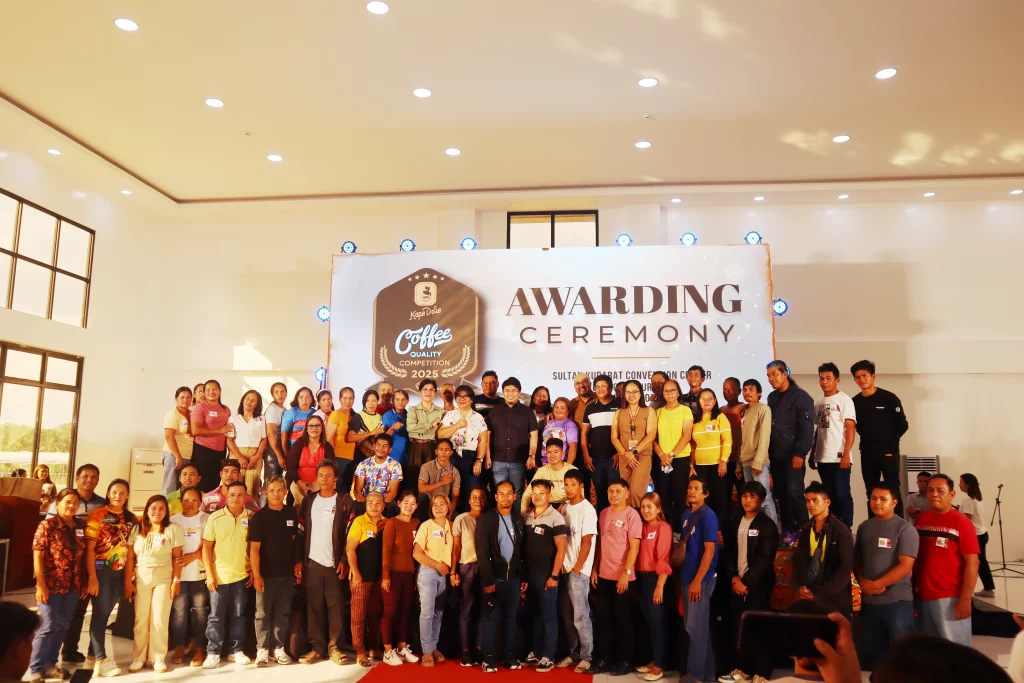 Participants, winners, organizers, and stakeholders gather for a group photo on stage in front of the official event banner during the Kape Dose 2025 Coffee Quality Competition Awarding Ceremony held in Sultan Kudarat.