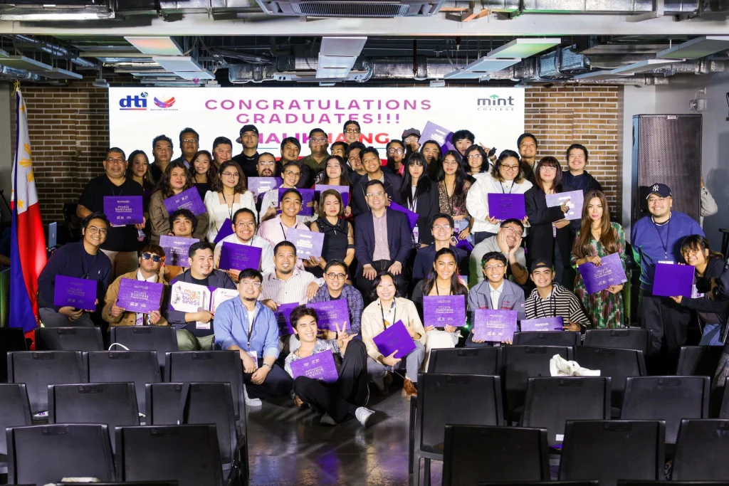 Graduates and organizers of the DTI-MINT College Malikhaing Pinoy: Music Business Masterclasses pose for a group photo, many holding certificates, under a "Congratulations Graduates" banner inside the MINT College Pasig Campus.