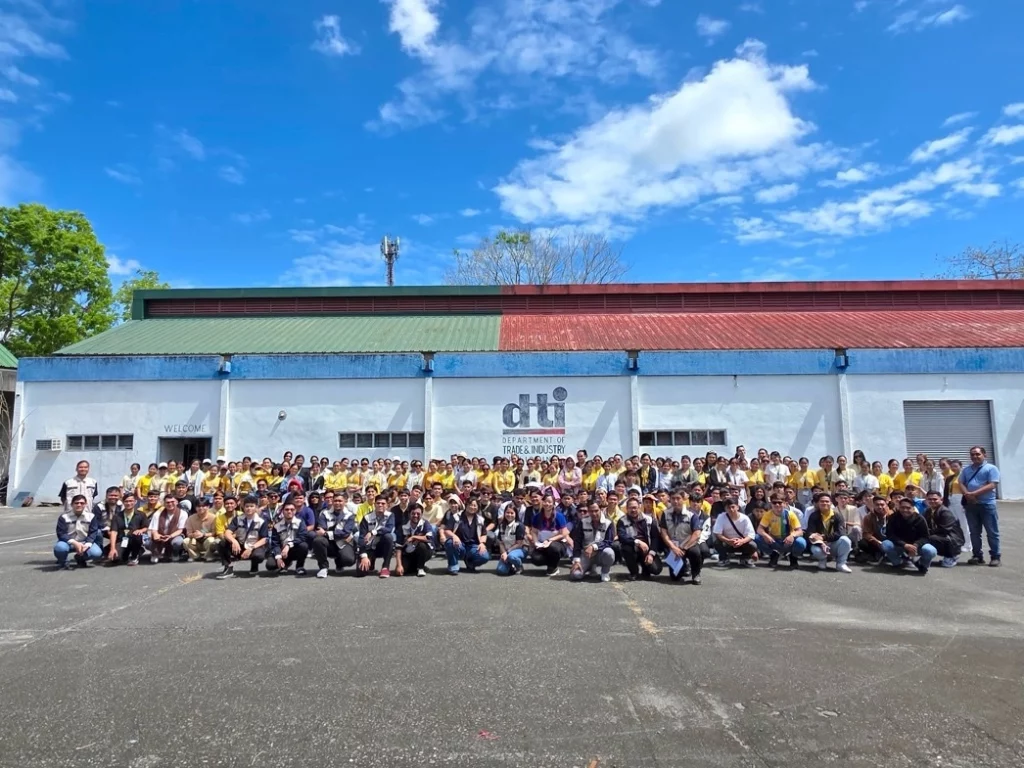 Wide-angle view of a large group of University of Northern Philippines (UNP) students posing for a photograph outdoors in front of the Department of Trade and Industry (DTI) building during their educational tour in Cavite.