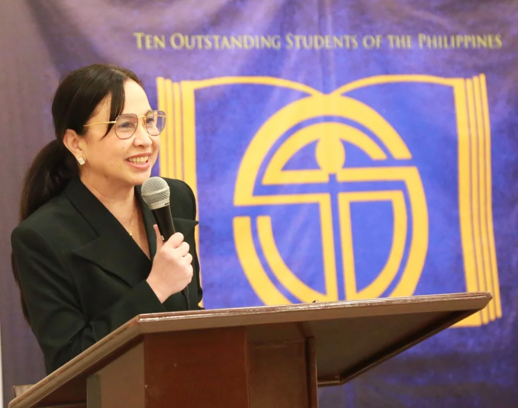 Department of Trade and Industry (DTI) Secretary Cristina A. Roque speaks at the 58th Ten Outstanding Students of the Philippines (TOSP) Honoring Ceremony. She is standing at a podium with a microphone, and the TOSP banner is visible behind her.