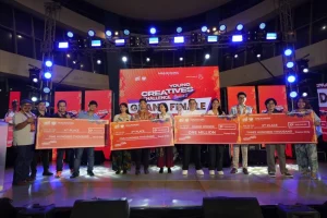 Young Creatives Challenge Grand Finale" event. The stage is brightly lit with multiple spotlights and a large red banner in the background displaying the event name. The checks have various amounts written on them, including "One Million," "Five Hundred Thousand," and "One Hundred Thousand.