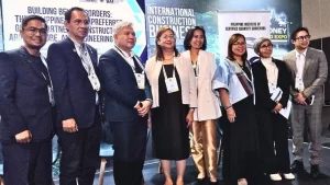 A group of delegates at the Philippines-Australia construction and engineering business mission event, standing in front of banners for the International Construction Business and the Philippine Institute of Certified Quantity Surveyors, wearing formal attire and event lanyards.