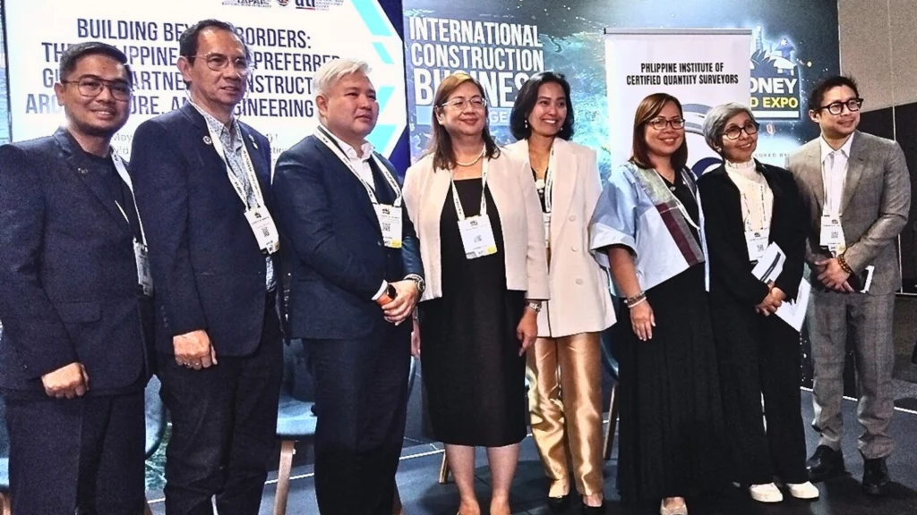 A group of delegates at the Philippines-Australia construction and engineering business mission event, standing in front of banners for the International Construction Business and the Philippine Institute of Certified Quantity Surveyors, wearing formal attire and event lanyards.