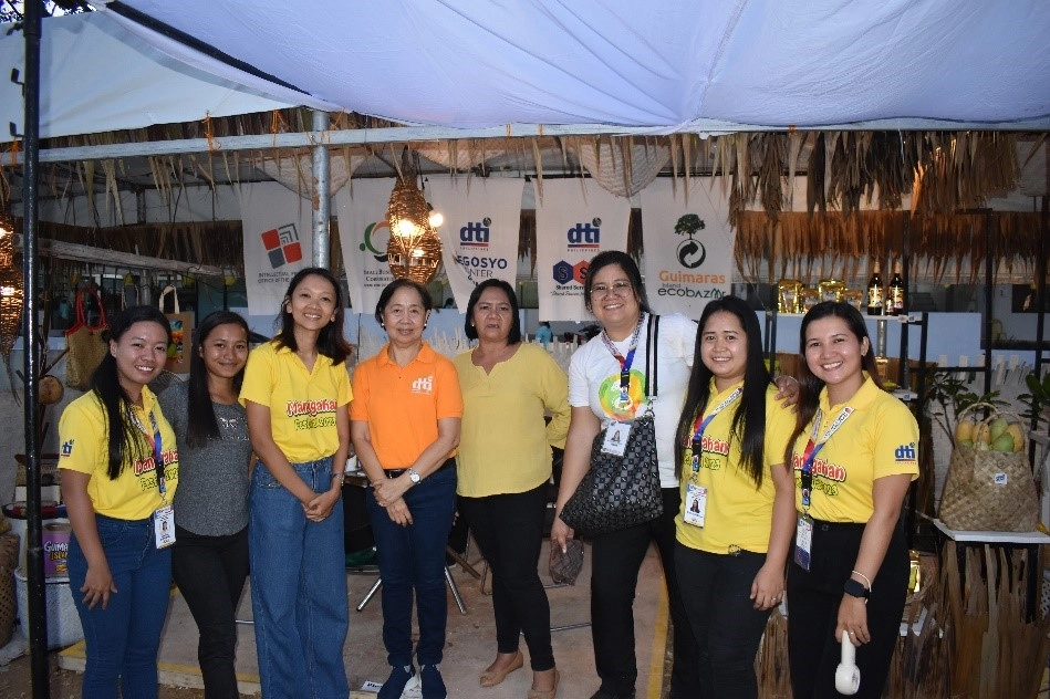DTI Region 6 and DTI Guimaras staff stand in front of a booth at the Manggahan Festival 2025 Trade Fair, promoting MSME products, processed mango goods, and offering business advisory services.