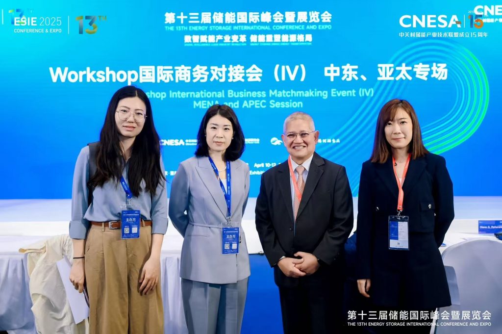 A medium shot of four people at a conference. The background shows a blue screen with conference information in English and Chinese.