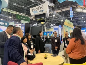 A group of people engage in conversation at an international trade show, with booths for companies like PilotFish, Solventium, and AWS visible in the background. The indoor exhibition hall features high ceilings and industrial lighting, reflecting the DTI’s global trade promotion efforts from January to May 2025 under the Philippine Export Development Plan.