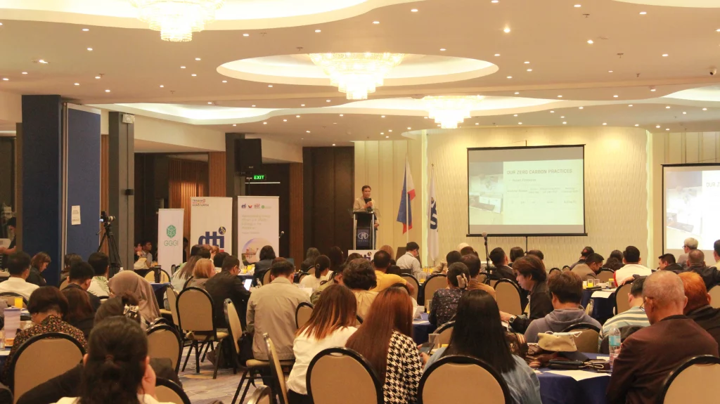 Attendees from various MSMEs and stakeholders across Mindanao seated at round tables during the DTI and GGGI energy efficiency investment roadshow at N Hotel, Cagayan de Oro, with a speaker presenting on stage and presentation slides displayed on large screens.