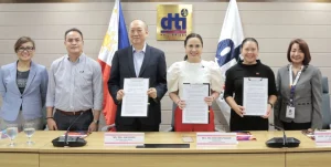 DTI Secretary Ma. Cristina A. Roque, Assistant Secretary Nylah Rizza D. Bautista, CIDO Director Lilian G. Salonga, Globaltronics CEO William T. Guido, Chief Revenue Officer Gary Reyes, and another official pose during the MOU signing ceremony to promote Filipino digital creatives, with Philippine and DTI flags in the background.