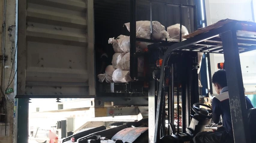 A worker uses a forklift to load large bags of substandard rubber inner tubes into a shipping container for re-export, as part of the DTI’s enforcement action at an industrial loading dock.