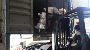 A worker uses a forklift to load large bags of substandard rubber inner tubes into a shipping container for re-export, as part of the DTI’s enforcement action at an industrial loading dock.