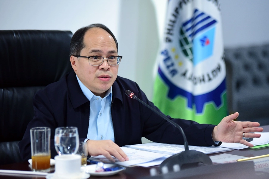 PEZA Director General Tereso O. Panga speaks into a microphone while seated at a table with documents and beverages, in front of a banner displaying the Philippine Economic Zone Authority (PEZA) logo. The setting reflects a formal event related to the DTI-led ecozone investment drive that secured PHP 66 billion by May 2025.