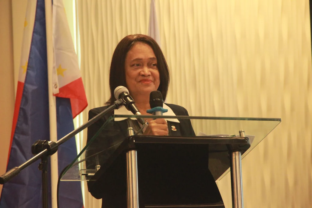 DTI Undersecretary Blesila Lantayona speaks at the podium during the energy efficiency investment roadshow in Cagayan de Oro, with the Philippine flag visible in the background.
