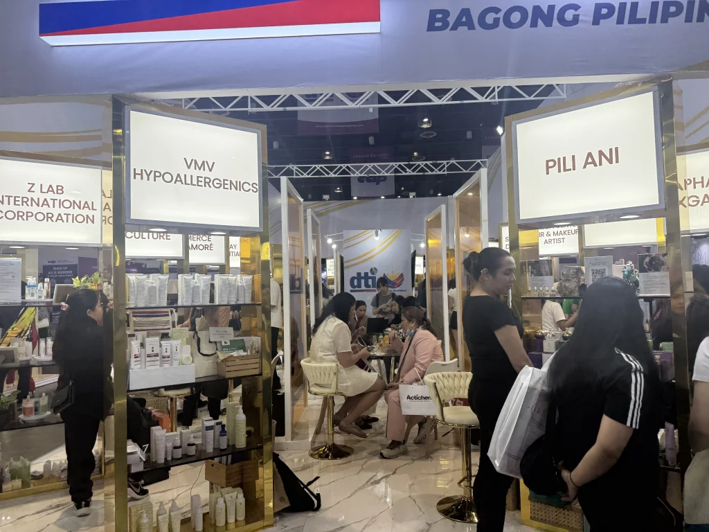 Exhibition booths of VMV Hypoallergenics and Pili Ani at Cosmobeauté Philippines 2025, with attendees exploring products and engaging in discussions under a 'Bagong Pilipinas' banner, showcasing Filipino MSMEs in the beauty industry.