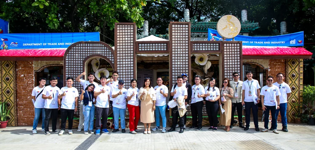 DTI staff and participants pose in front of a decorated Department of Trade and Industry booth at the Pampamahalaang Programa at Serbisyo 2025 in Rizal Park. The booth, adorned with traditional Filipino elements, showcases the agency’s support for MSMEs and the Tatak Pinoy initiative during the Independence Day celebration.