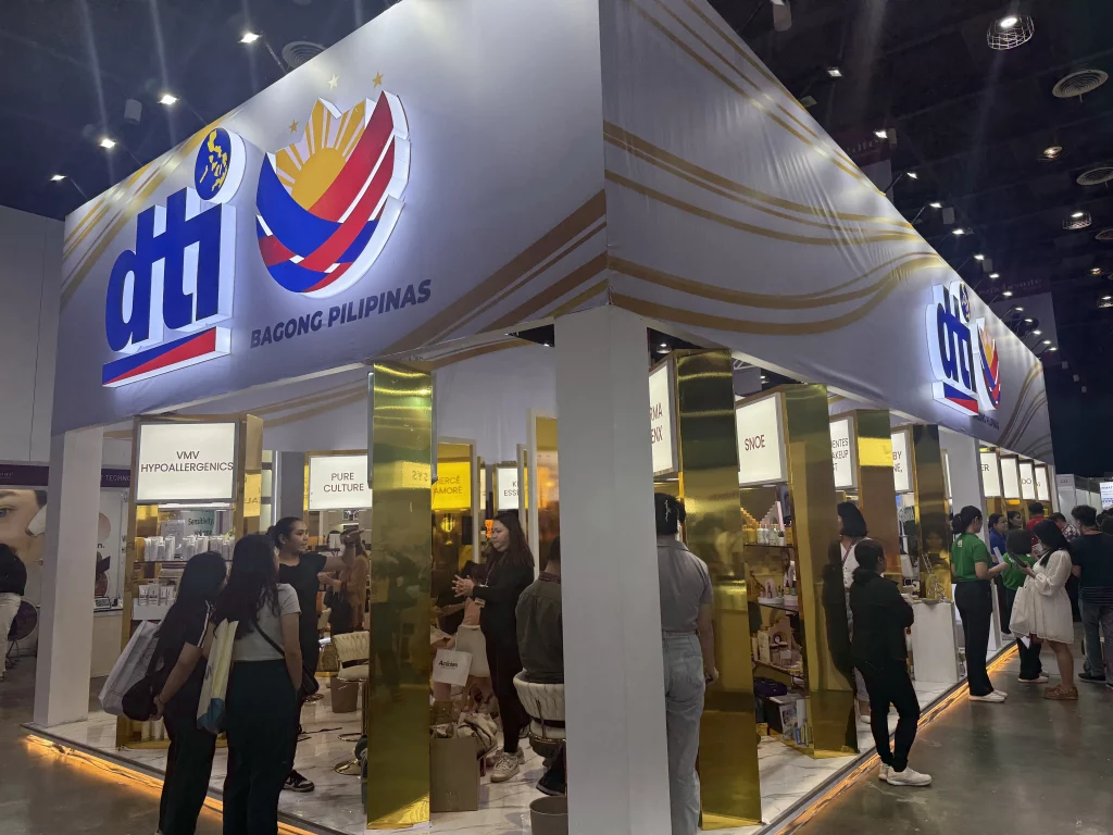 DTI Philippines booth at Cosmobeauté Philippines 2025, featuring gold-accented displays, the 'Bagong Pilipinas' banner, and various product showcases, with attendees interacting with exhibitors.