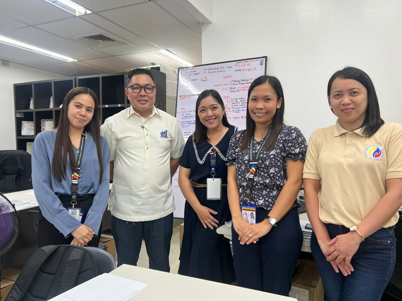 Jojo F. Toledo IV, Supervising Trade-Industry Development Specialist, and Kris T. Pascual, Trade-Industry Development Analyst of the SME Development Division, DTI Region 3, together with Jollie Q. Fell, OIC-Chief and Supervising Labor and Employment Officer; Honey Lyn U. Piñol and Christine R. Gregorio, both Labor and Employment Officers II of the Department of Migrant Workers-Region 3, standing in an office setting with a whiteboard in the background displaying various notes.