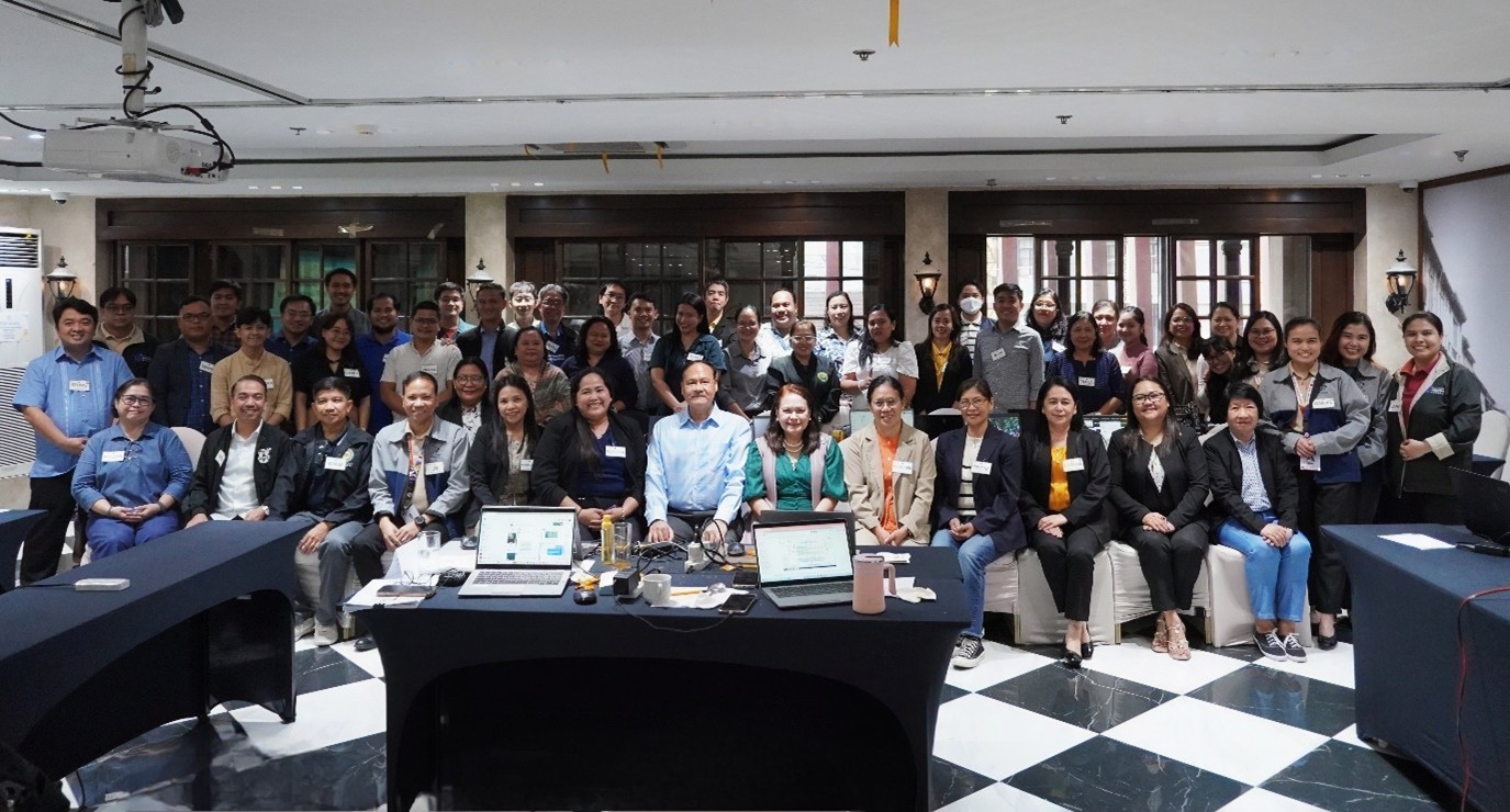 Group photo of participants during the DTI-PAB ISO 21001 Educational Organizations Management System (EOMS) training workshop, showing around 40 attendees in a conference room with tables, laptops, and workshop materials.